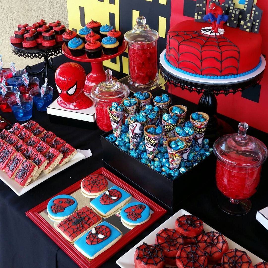 Spiderman themed dessert table with red webbed cake, cookies, and blue cupcakes