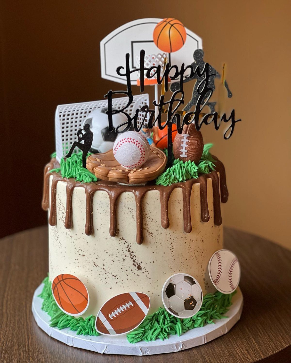 Sports themed birthday cake with chocolate drips and miniature balls and toppers.