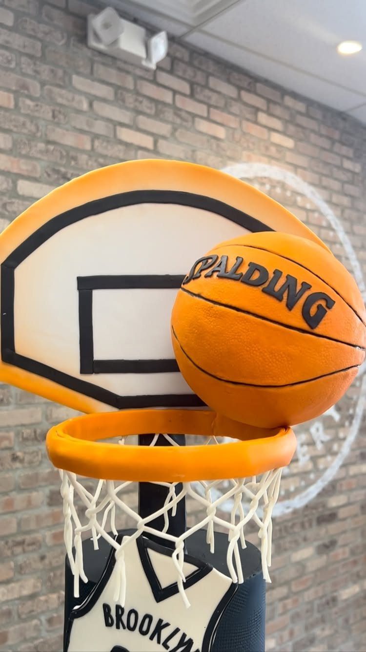 Basketball themed cake with a 3D ball, hoop, and backboard on brick background