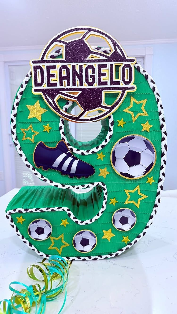 Number 9 shaped green soccer piñata decorated with balls, stars, and a name topper.