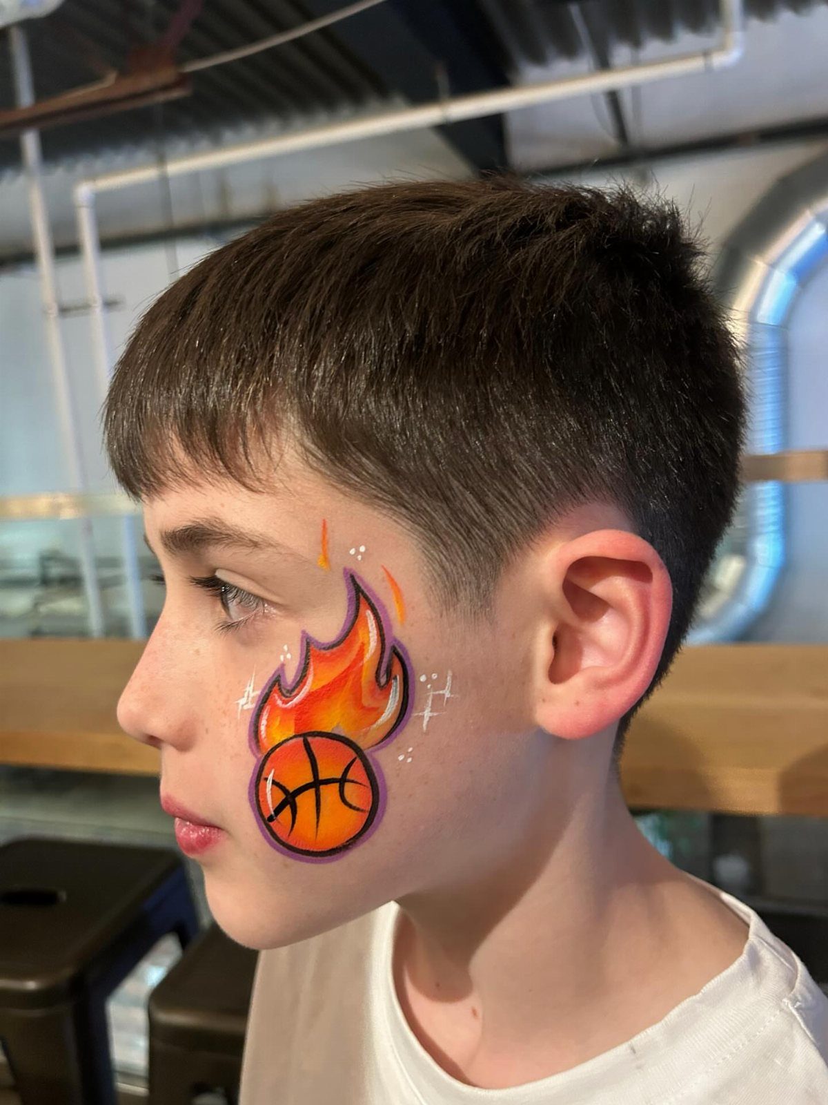 Young boy with a flaming basketball painted on his cheek in profile view.