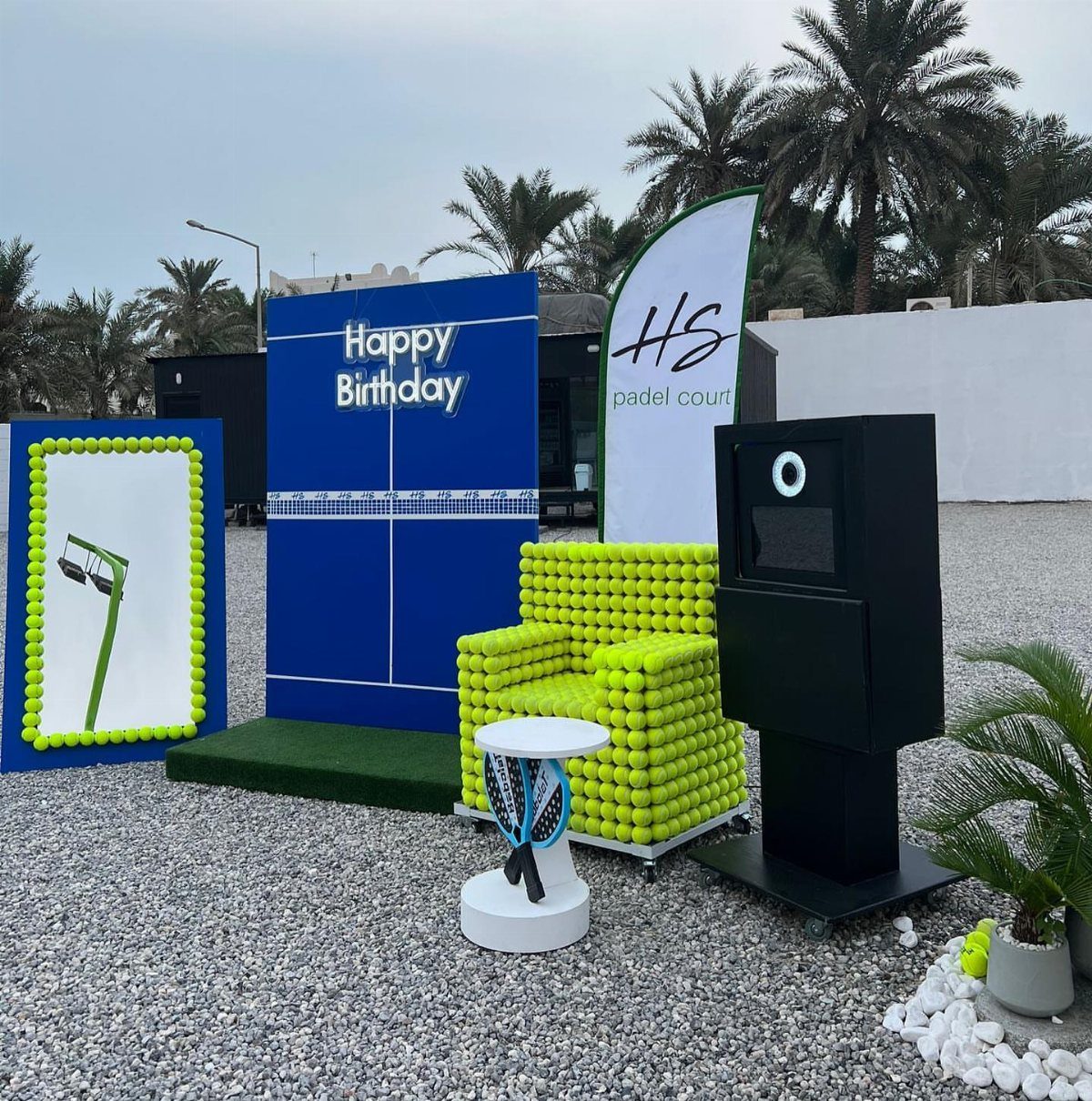 Sports-themed photo booth setup with tennis ball chair and birthday backdrop outdoors.