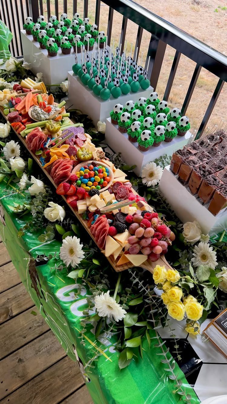Fruit and cheese platter with soccer ball themed cupcakes on a party table.