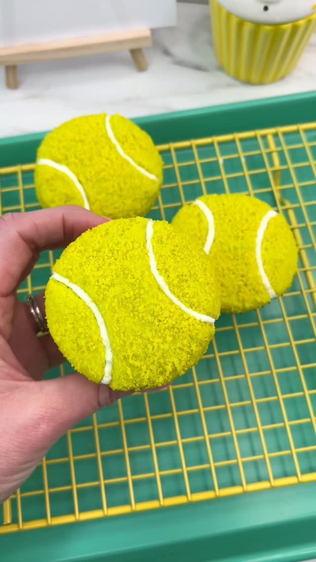 Tennis ball cake pops on a yellow wire rack over a teal tray.
