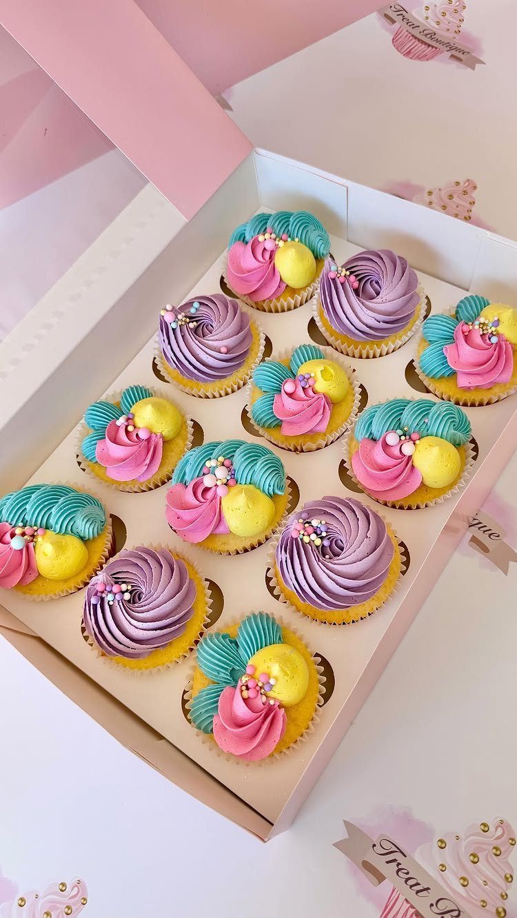 Colorful frosted cupcakes with silver pearls in a white bakery box.