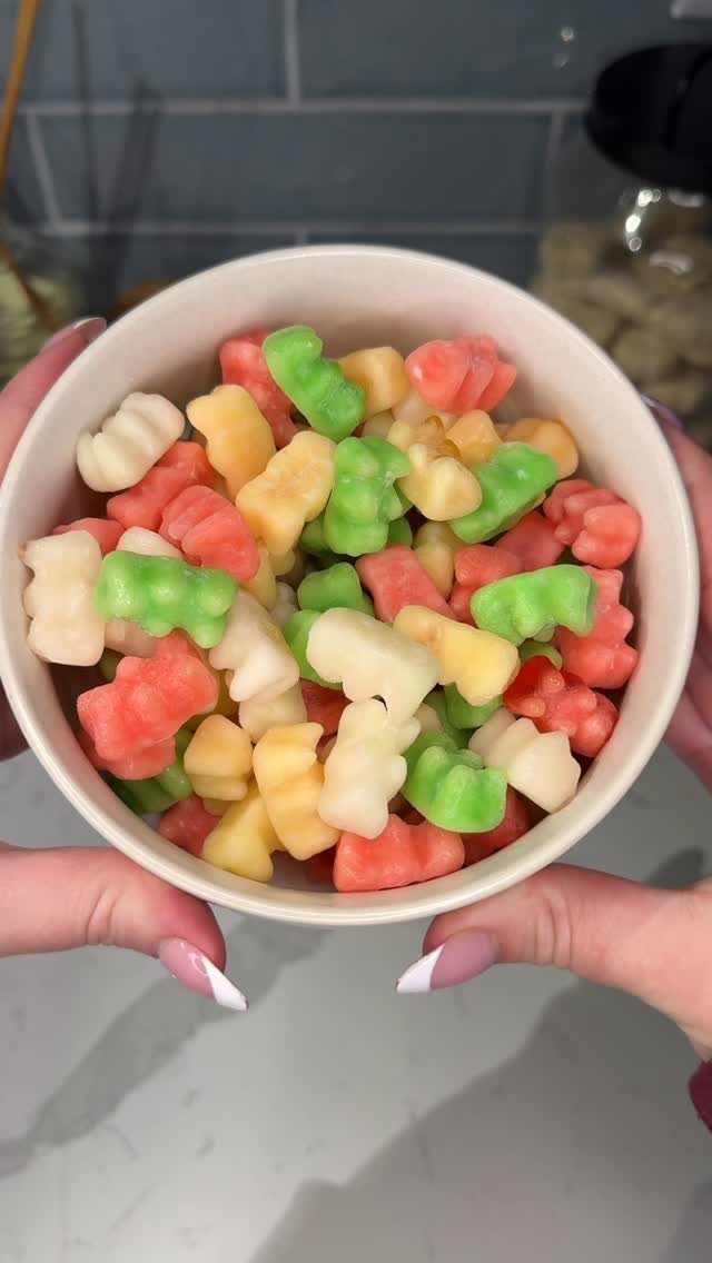 White bowl of colorful gummy bears held by hands with white nails.