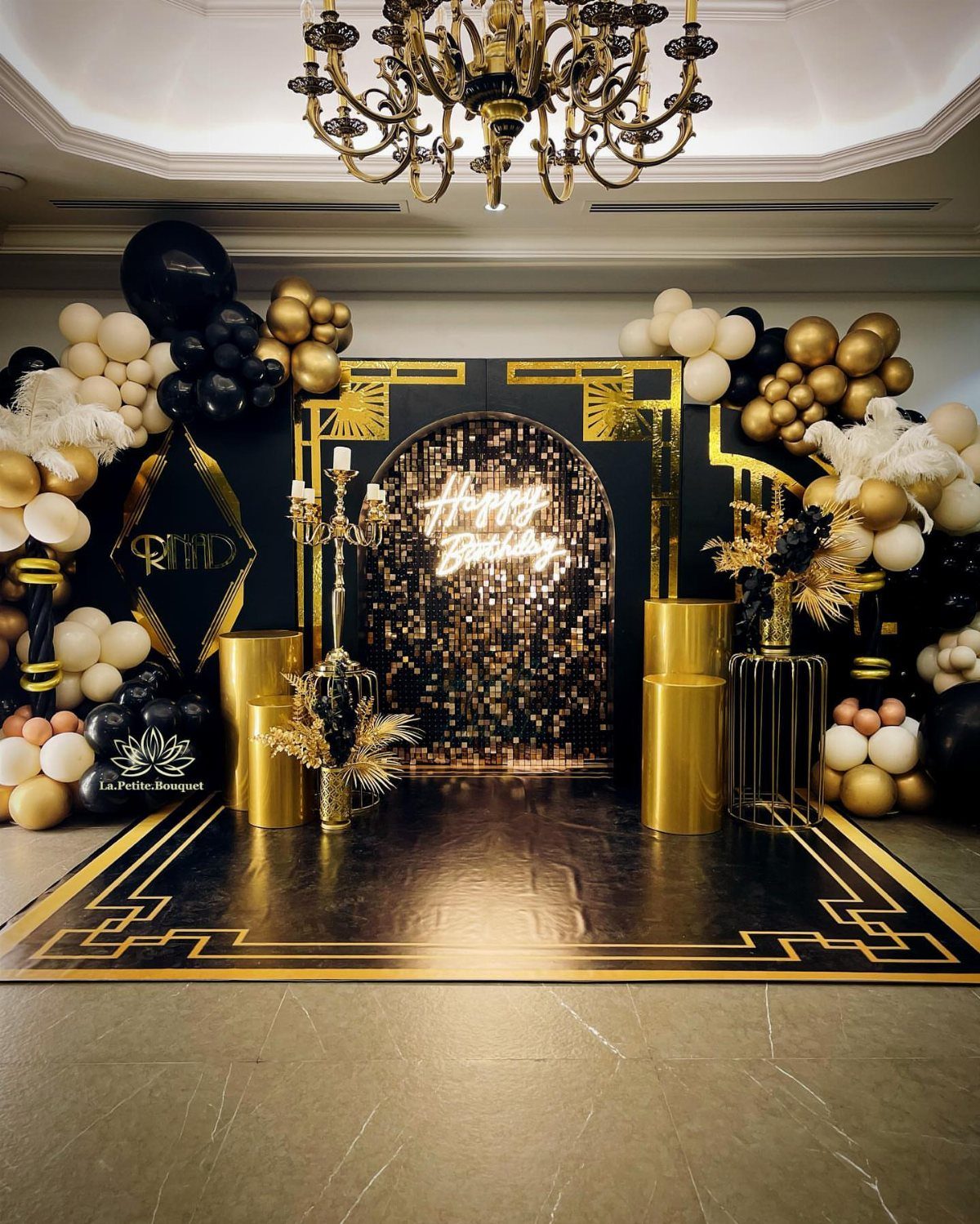 Black and gold party decor with balloons, pedestals, and a shimmering backdrop.