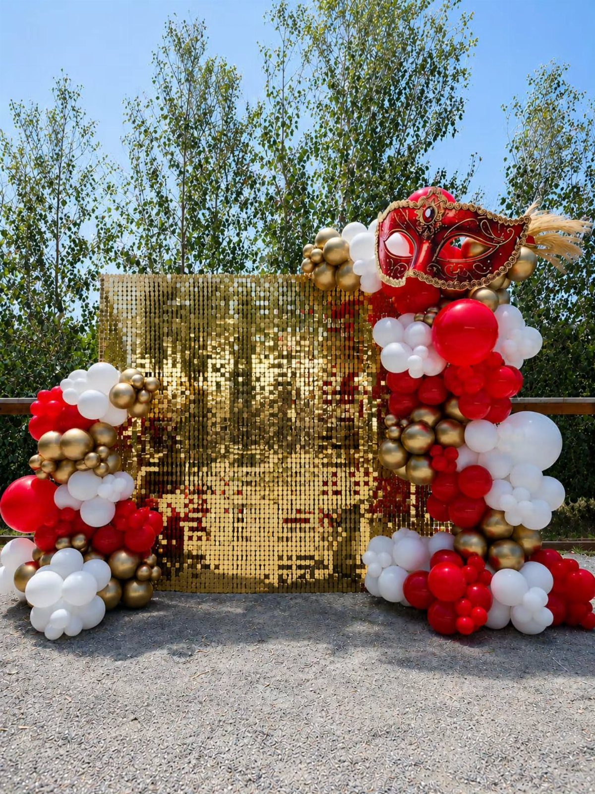 Gold sequin backdrop with red and white balloons and a masquerade mask.