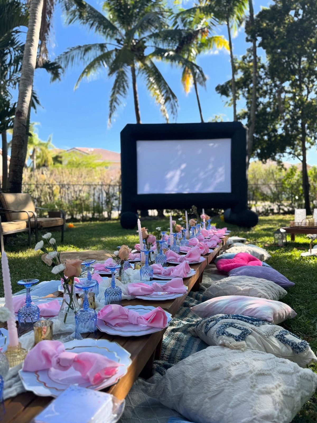 Outdoor movie setup with a low table, pink napkins, and floor cushions.