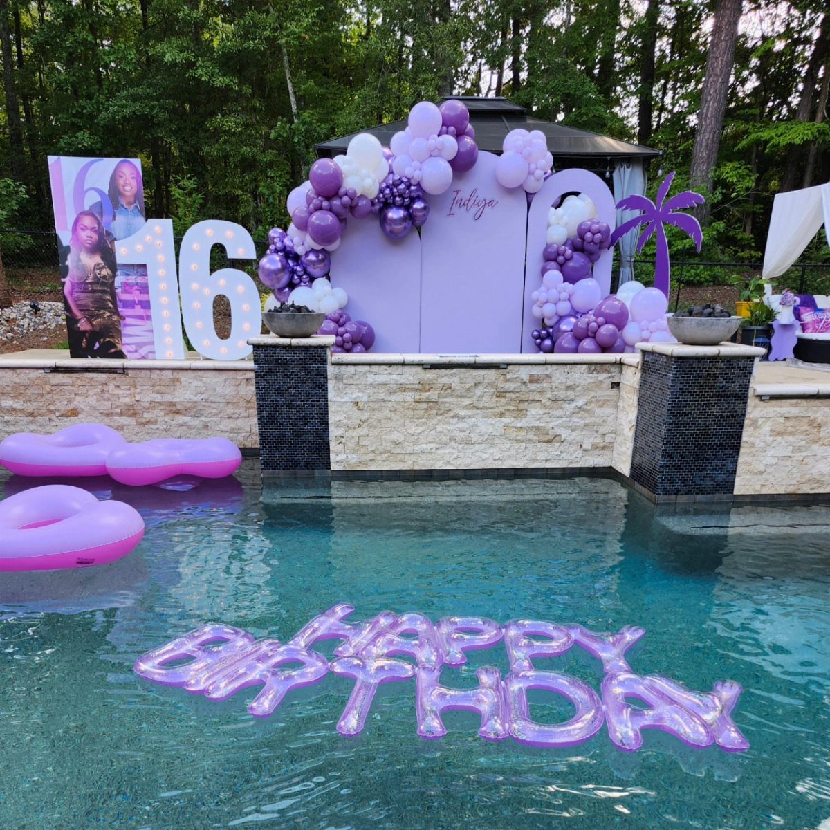 Poolside birthday party setup with purple balloons, white 16 sign, and floating letters.