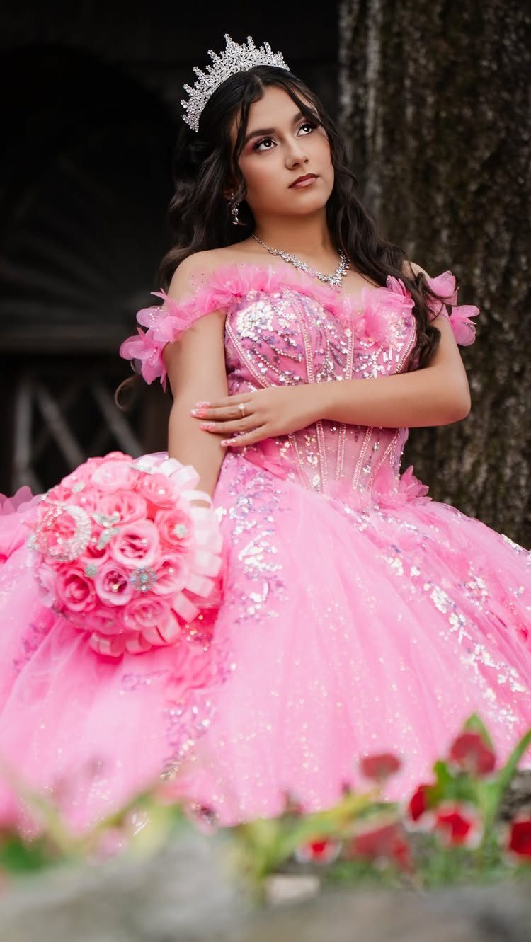 Young woman in a pink sparkling ballgown and tiara holding pink roses outdoors.