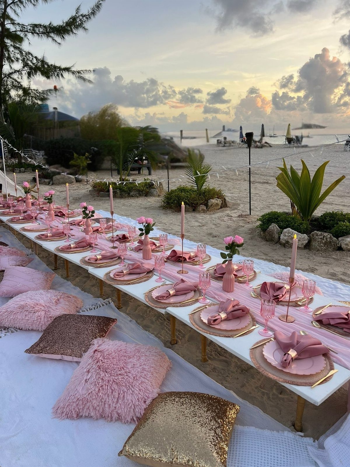 Low white dinner table with pink decor and pillows on a sandy beach