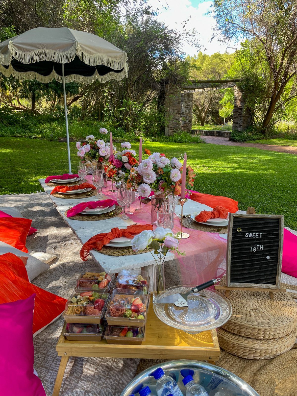 Outdoor picnic table with pink decor, flowers, and a Sweet 16th chalkboard sign.