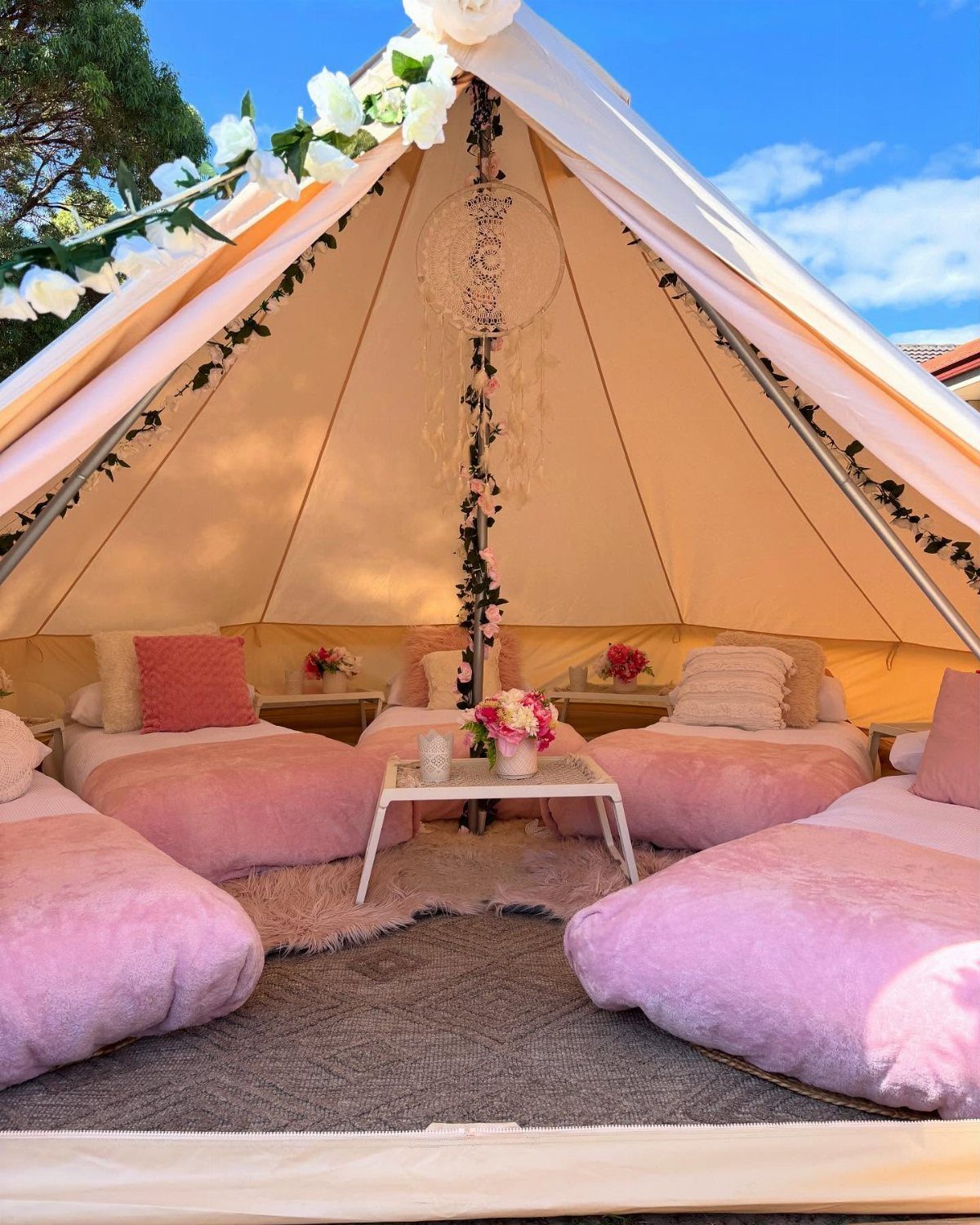 Interior of a decorated bell tent with pink bedding and floral accents.