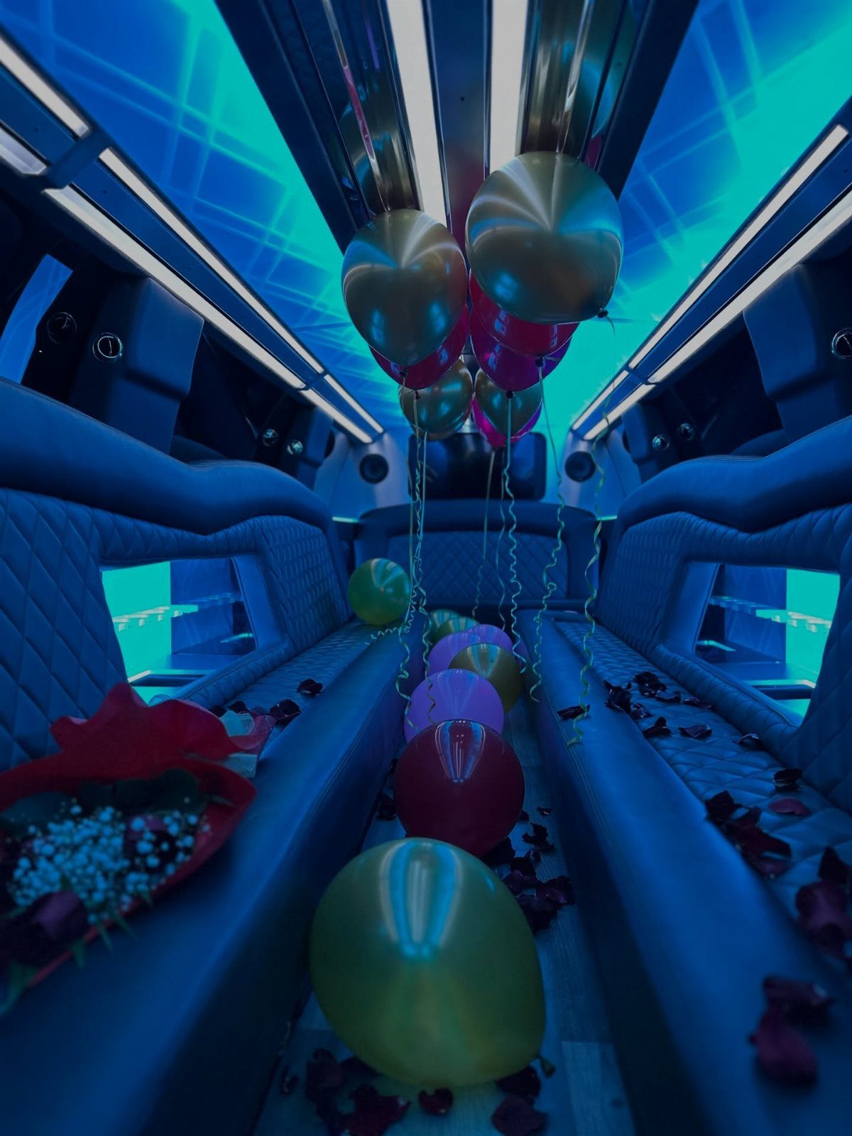 Limousine interior with blue neon lights, gold balloons, and red rose petals.