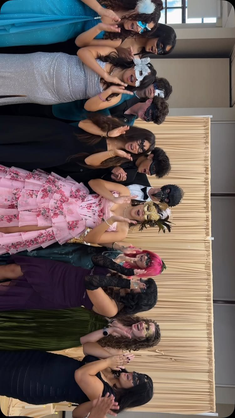 Group of people in formal wear and masquerade masks posing against a curtain.