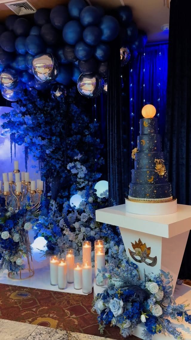 Blue themed party decor with a tiered cake, balloon arch, and white candles.