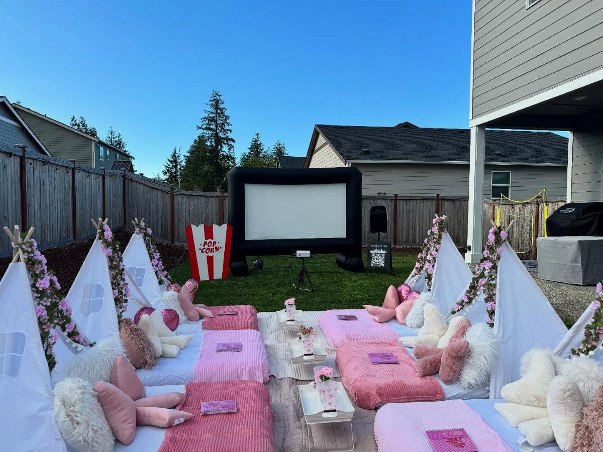 Outdoor movie setup with white teepees, pink bedding, and a large inflatable screen.