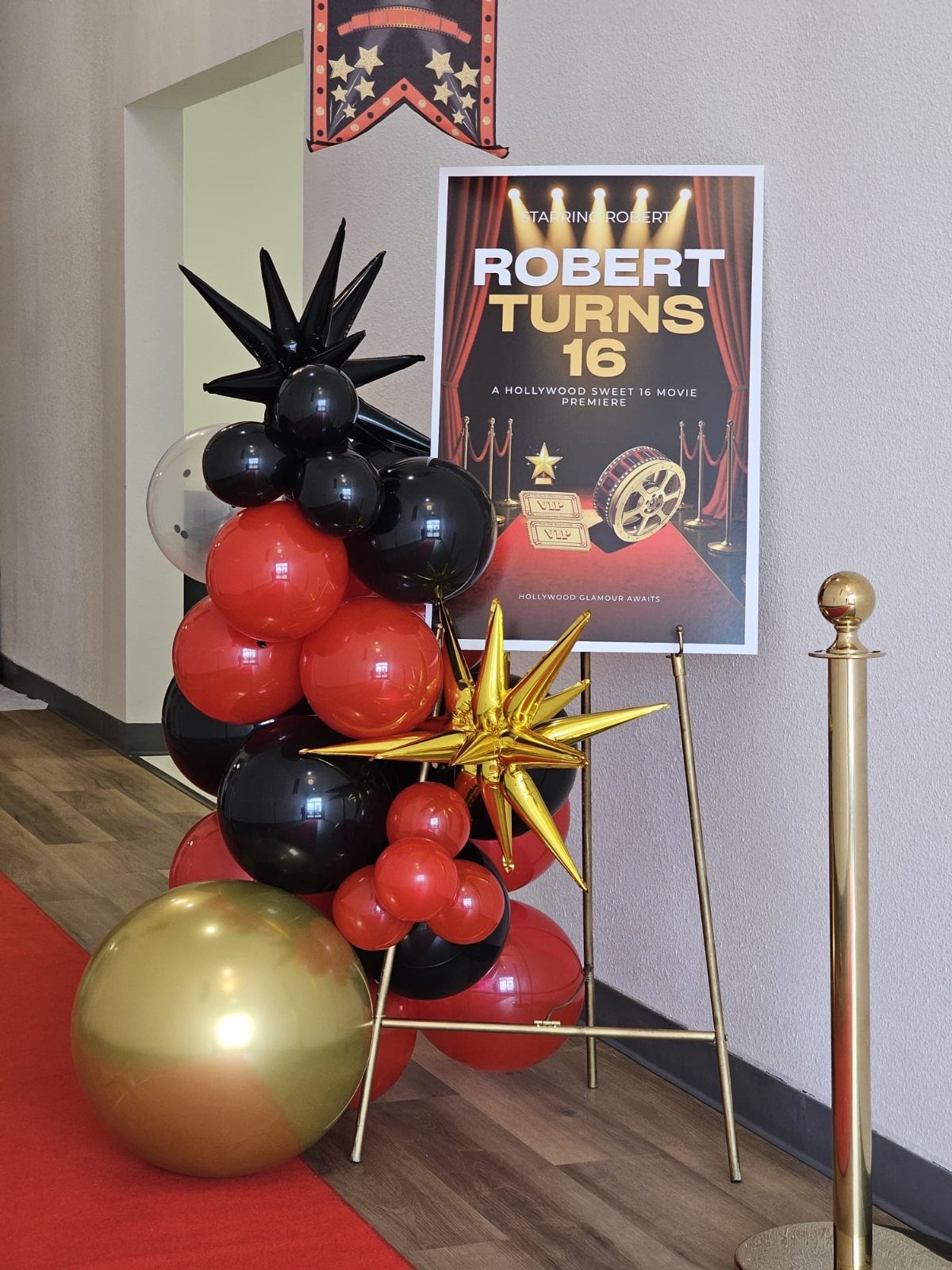 Red carpet entrance with red, black, and gold balloons and a birthday poster.