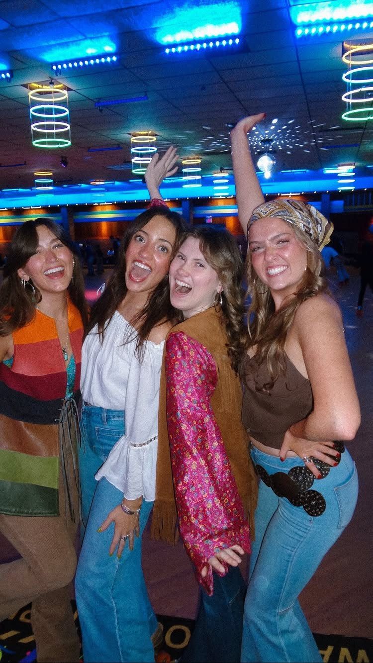Four teenage girls in retro clothing posing inside a neon lit roller rink.