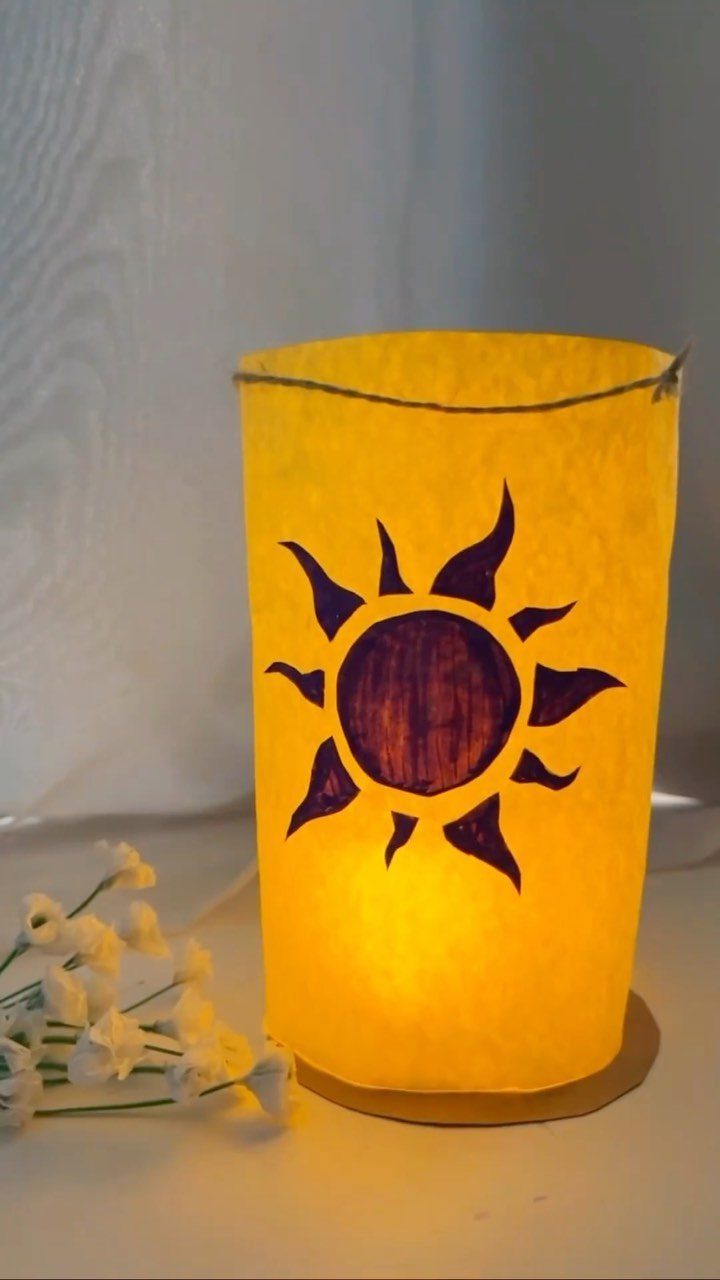 Yellow paper lantern with a purple sun symbol glowing on a white surface.