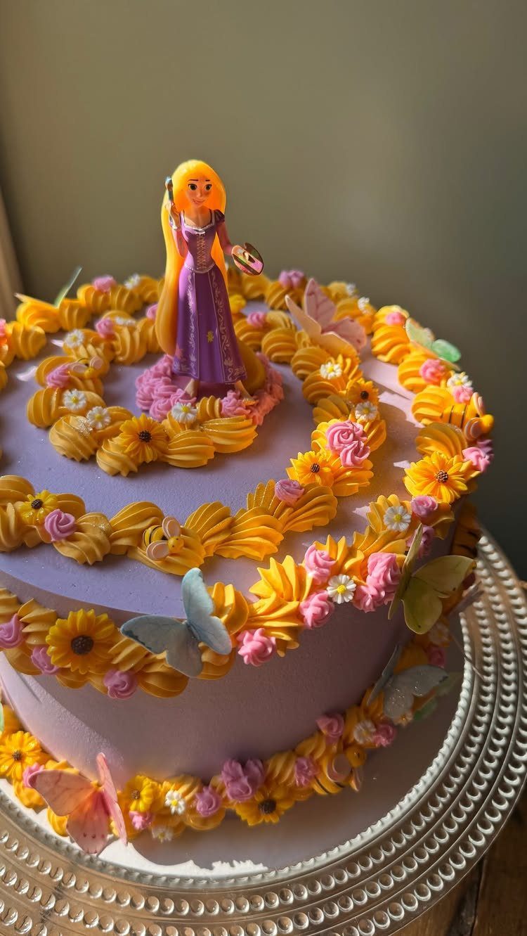 Purple cake with yellow frosting flowers and a Rapunzel figurine on top.