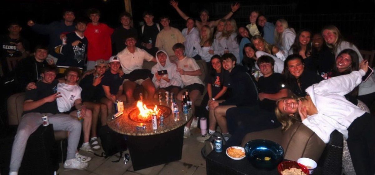 Group of teenagers gathered around a glowing outdoor fire pit at night.