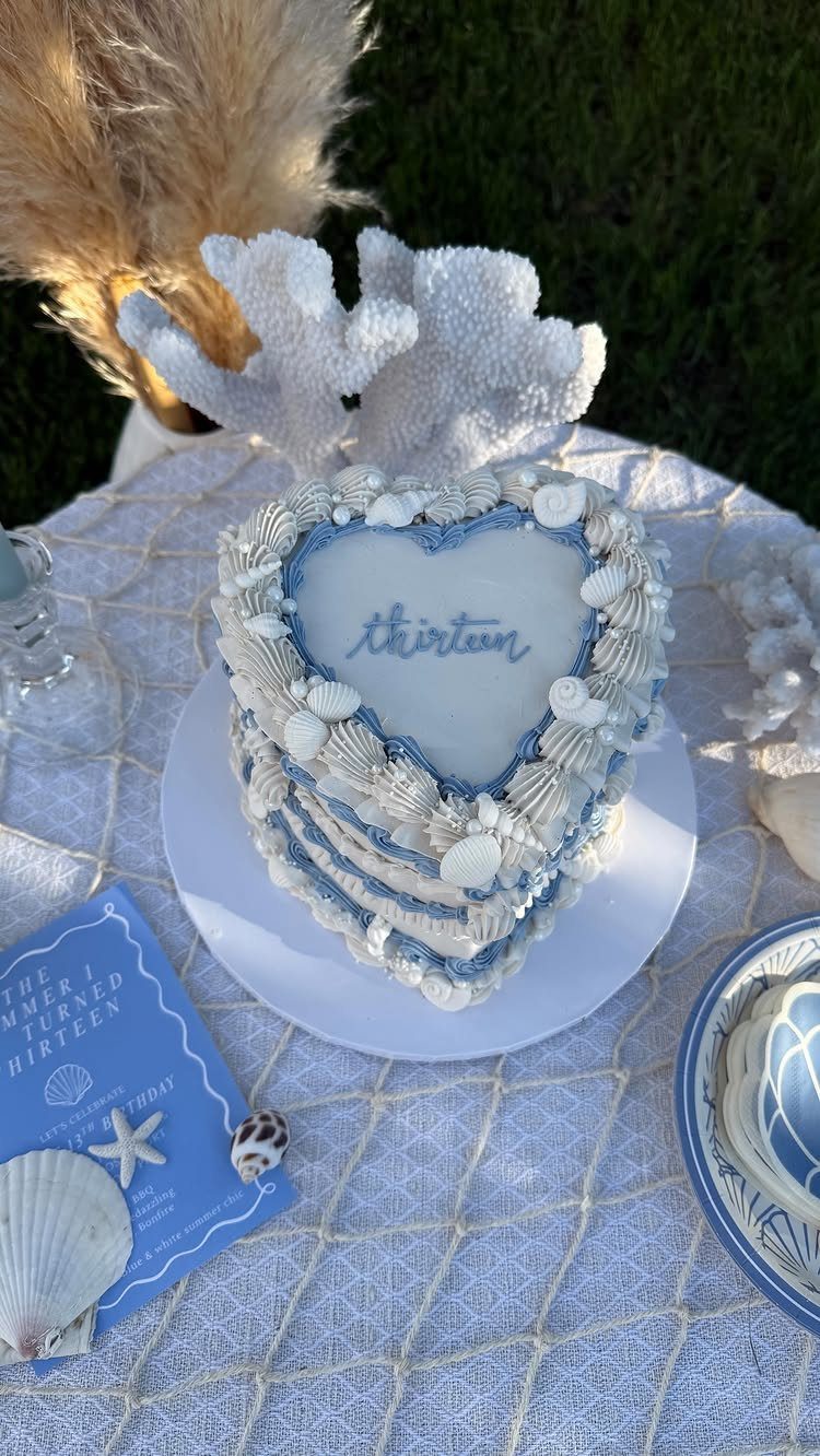 Heart-shaped blue and white cake with seashells for a thirteenth birthday beach party.