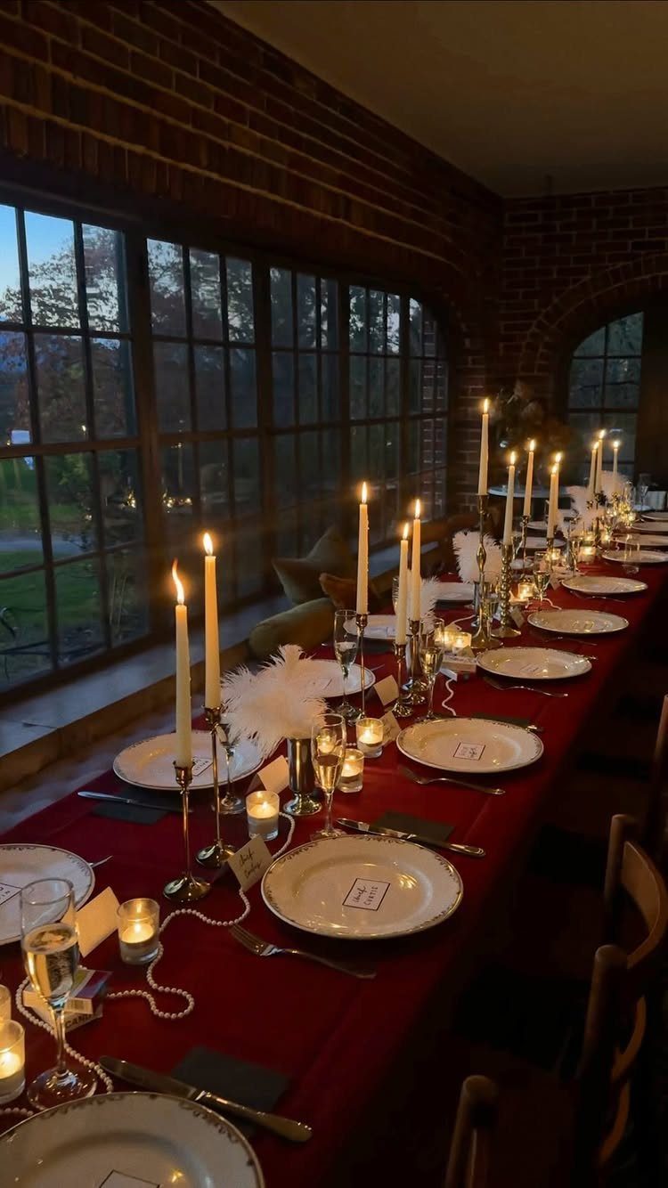 Elegant dinner table with red cloth and lit candles in a brick room.
