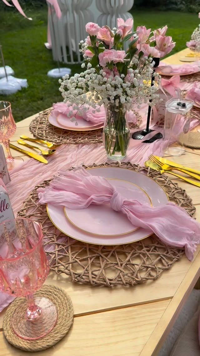 Elegant outdoor table setting with pink plates, gold cutlery, and pink floral centerpieces.