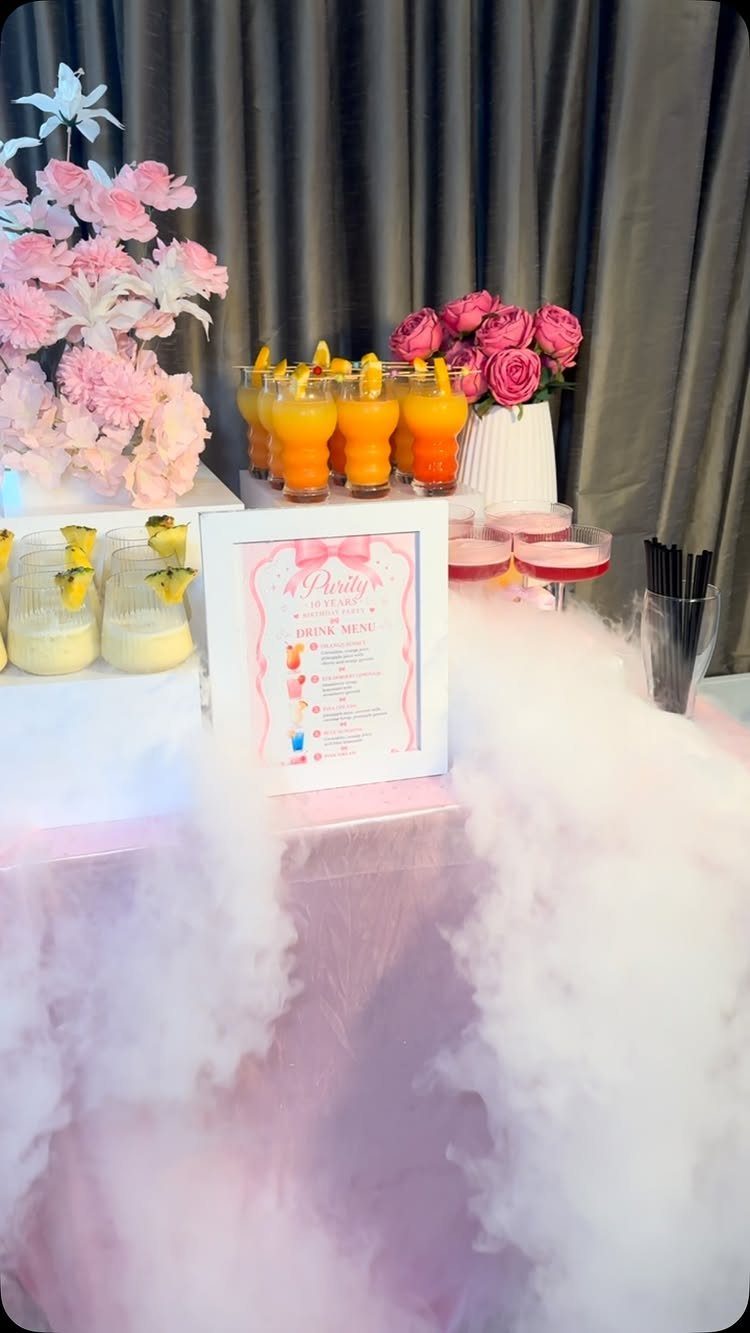 Pink party table with orange mocktails, floral arrangements, and a drink menu.