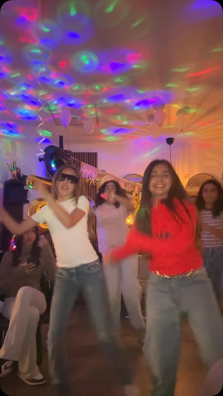 Teenage girls dancing in a room with colorful disco lights on the ceiling.