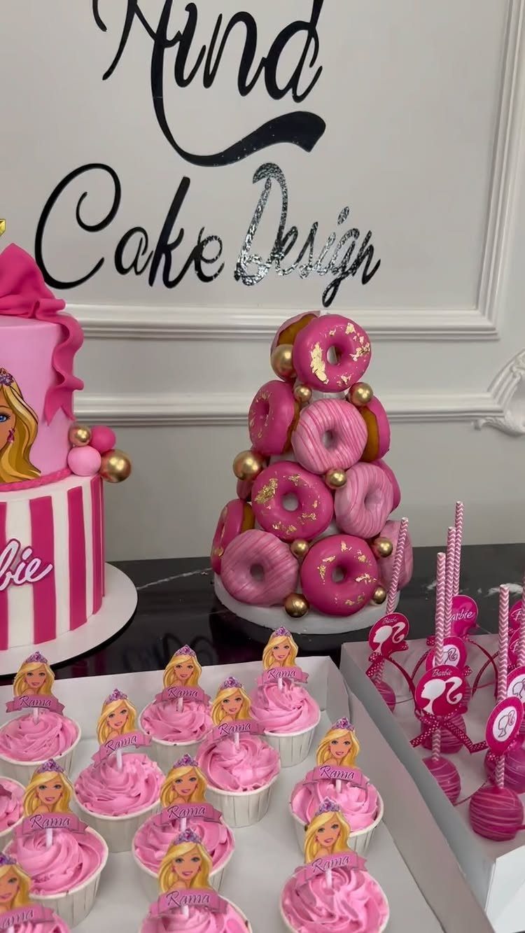 Pink Barbie themed cake, donut tower, and cupcakes on a white dessert table.