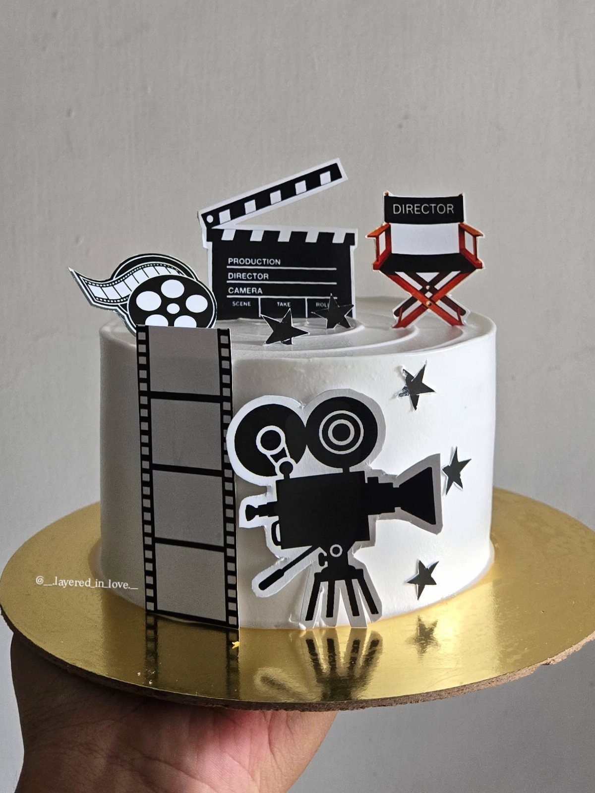 White frosted cake decorated with movie camera, clapperboard, and director's chair toppers.