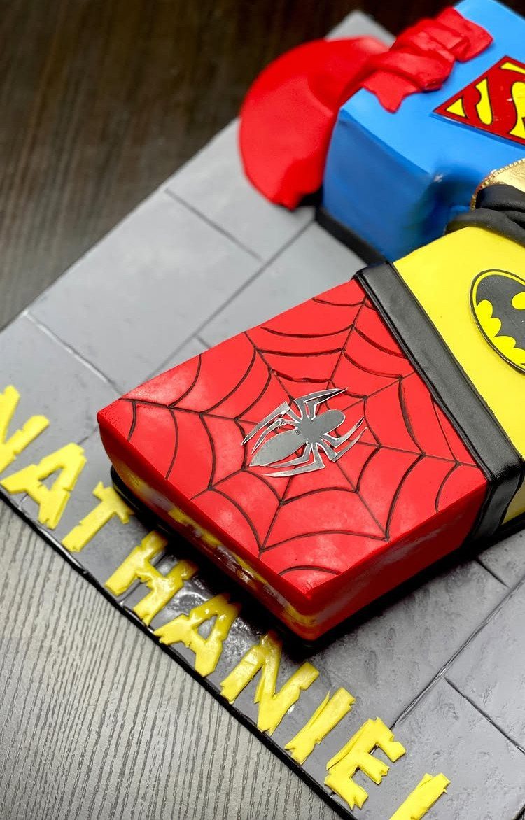 Superhero themed cake designed as comic books with Spider-Man, Batman, and Superman logos.