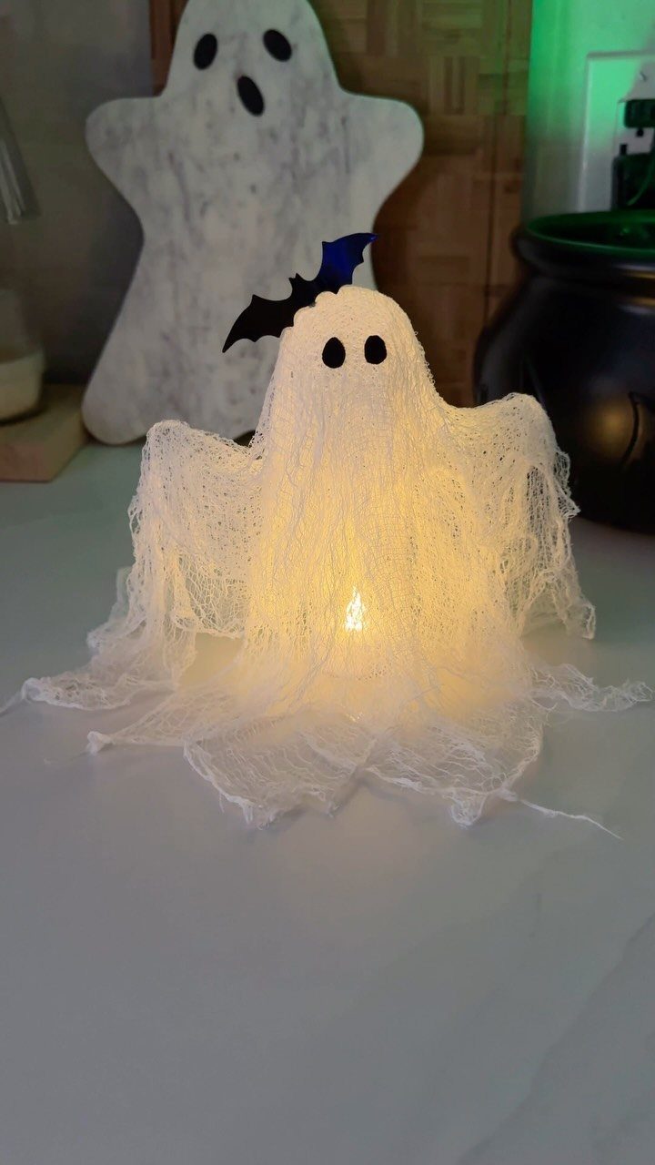 Glowing white fabric ghost decoration with a small blue bat on top.