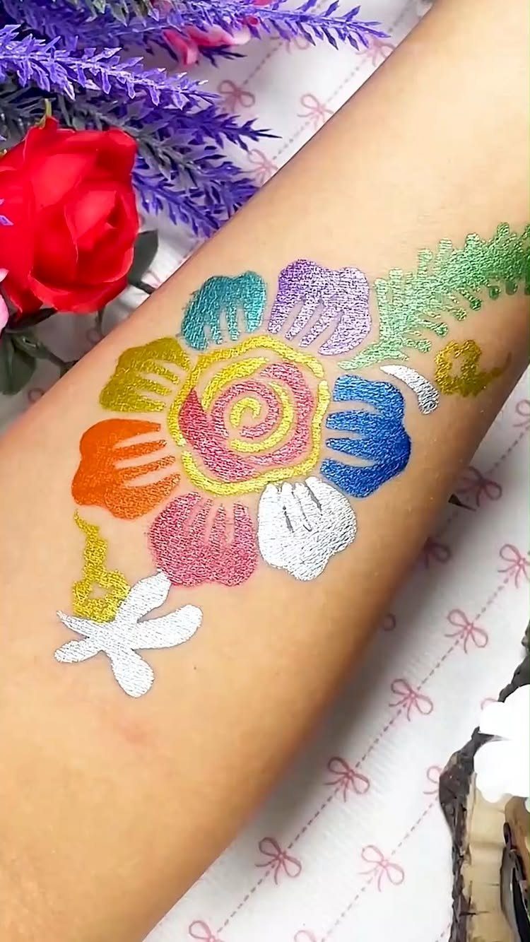 Colorful glittery floral body art painted on a person's arm with flowers nearby