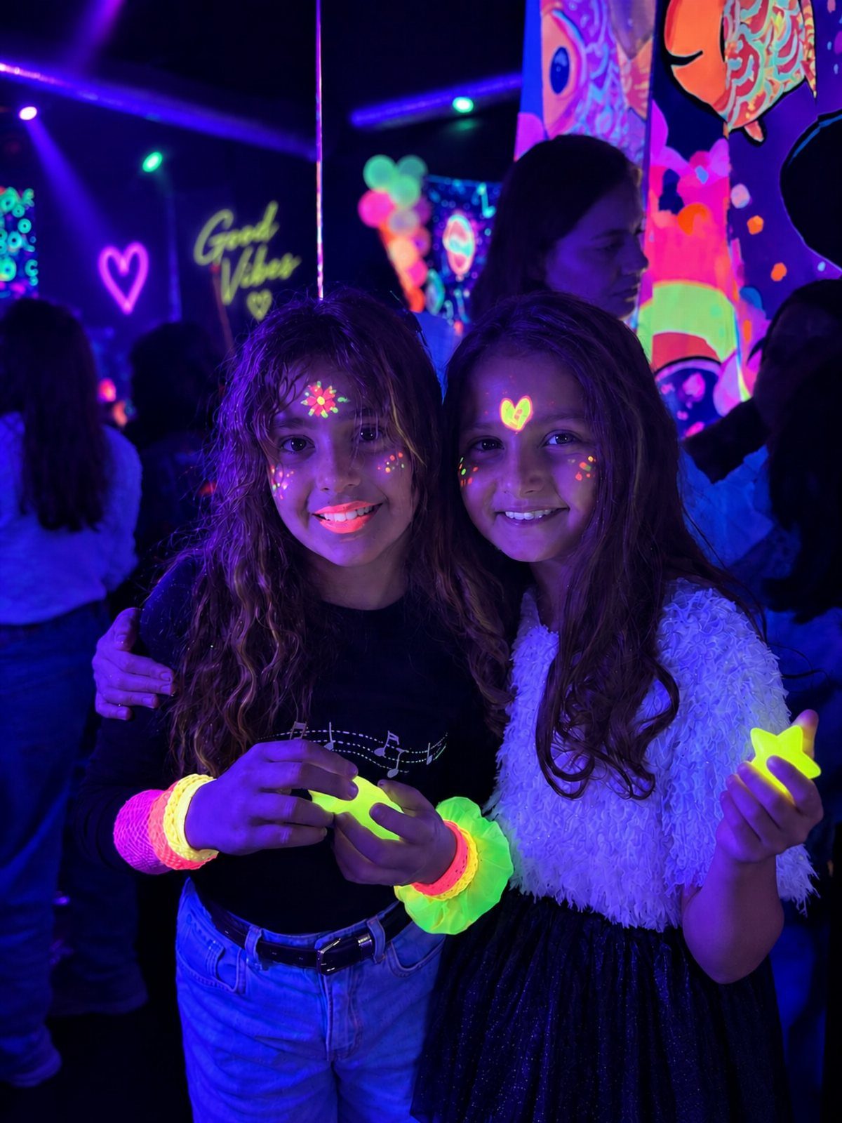 Two girls with neon face paint and glow sticks at a glow party.
