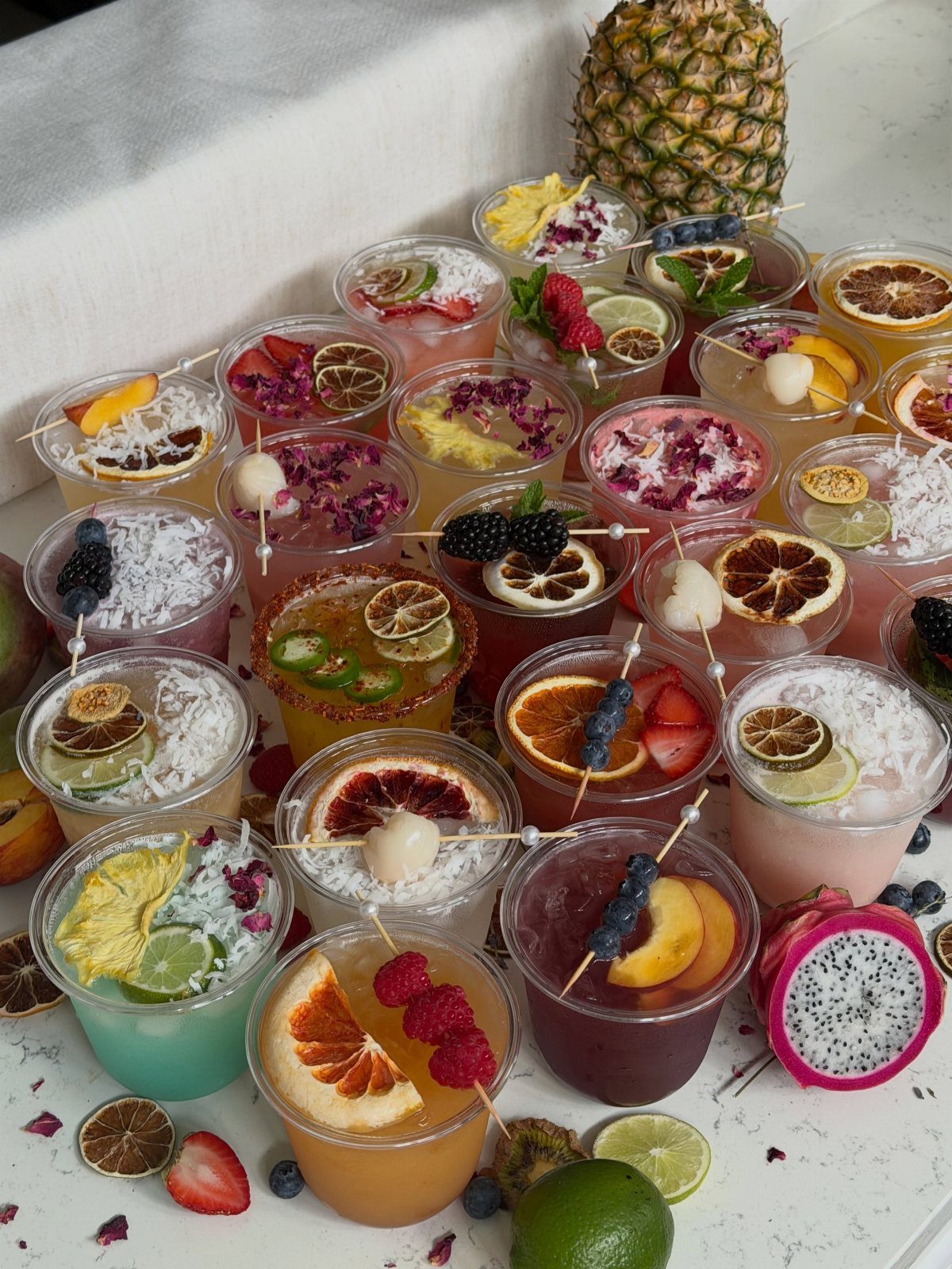 Colorful mocktails in clear cups garnished with fresh fruit on a white table