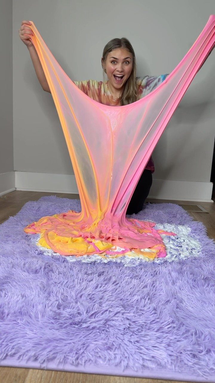 Young woman stretching a large sheet of colorful pink and orange slime.