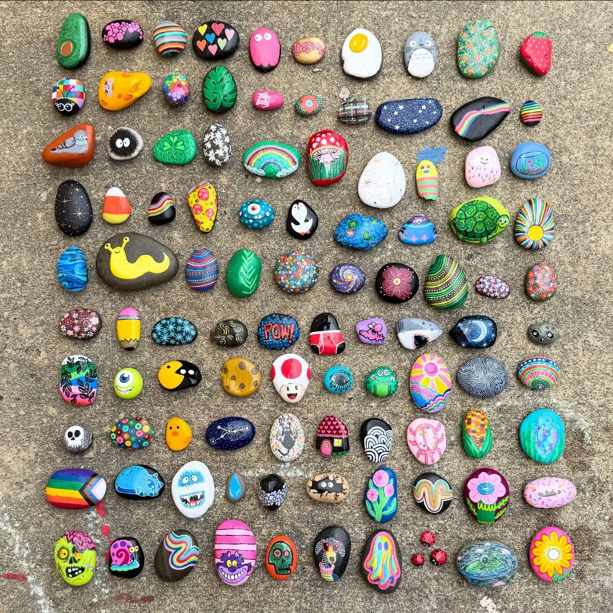 Many small stones painted with colorful animals and patterns on a concrete floor.