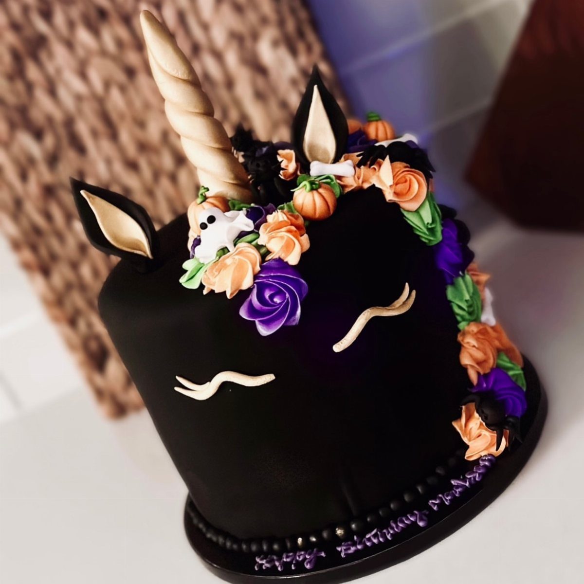 Black unicorn cake with gold horn and orange, purple, and green frosting roses.