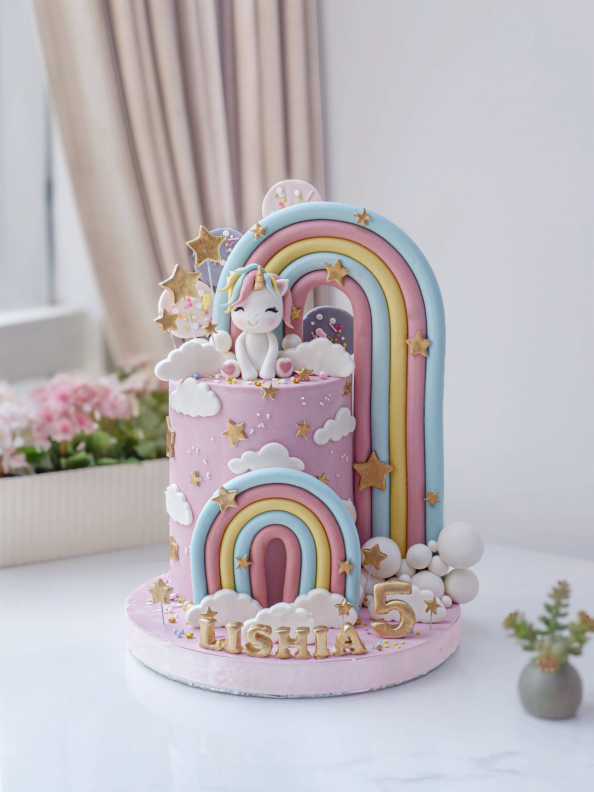 Pink unicorn birthday cake with pastel rainbows, gold stars, and a unicorn figurine.