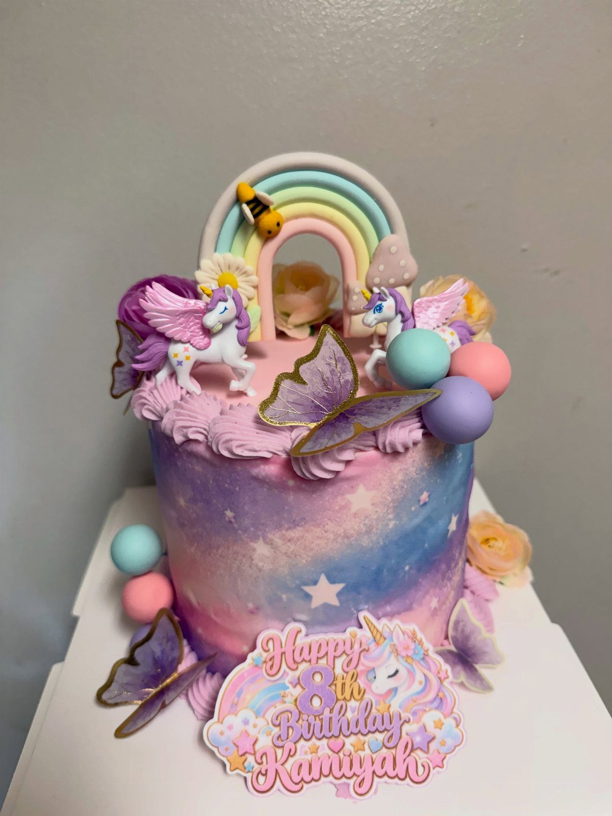 Galaxy cake with purple frosting, unicorn figurines, a rainbow, and birthday plaque.