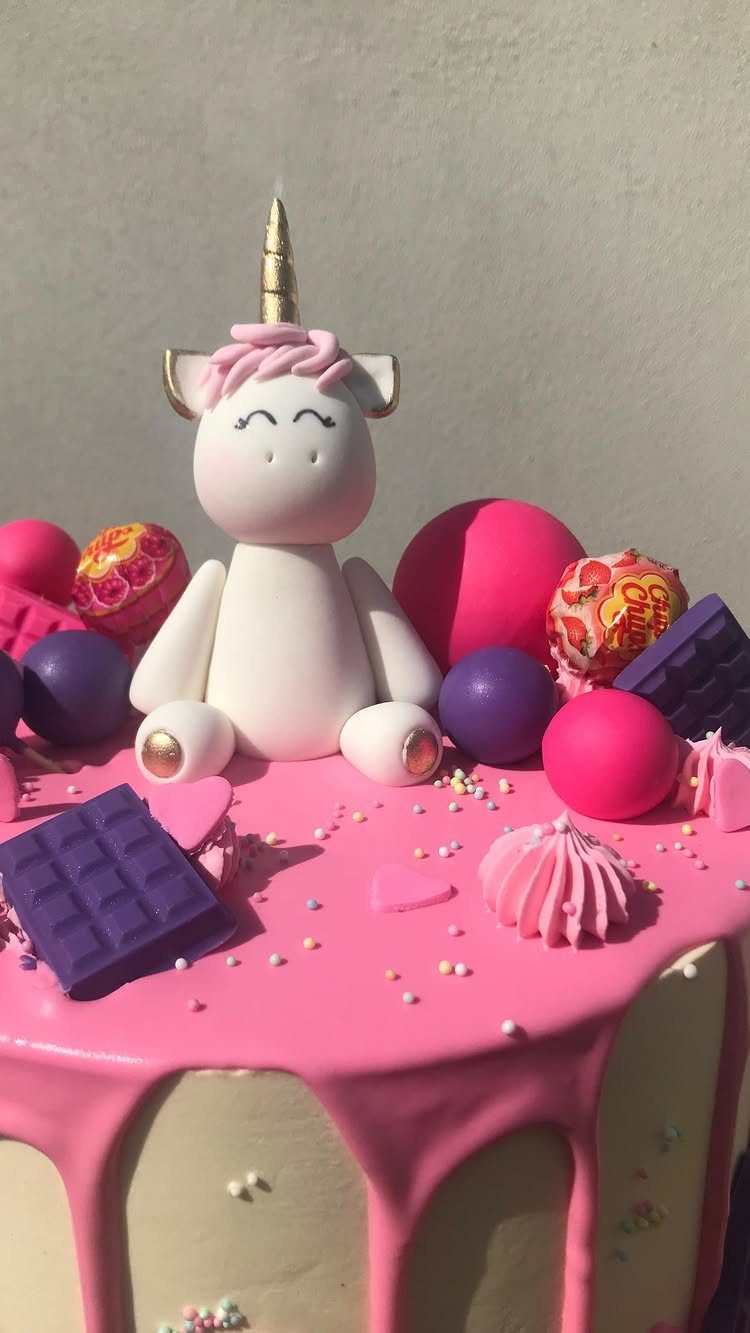 White cake with pink drip frosting topped with a small white unicorn figurine.