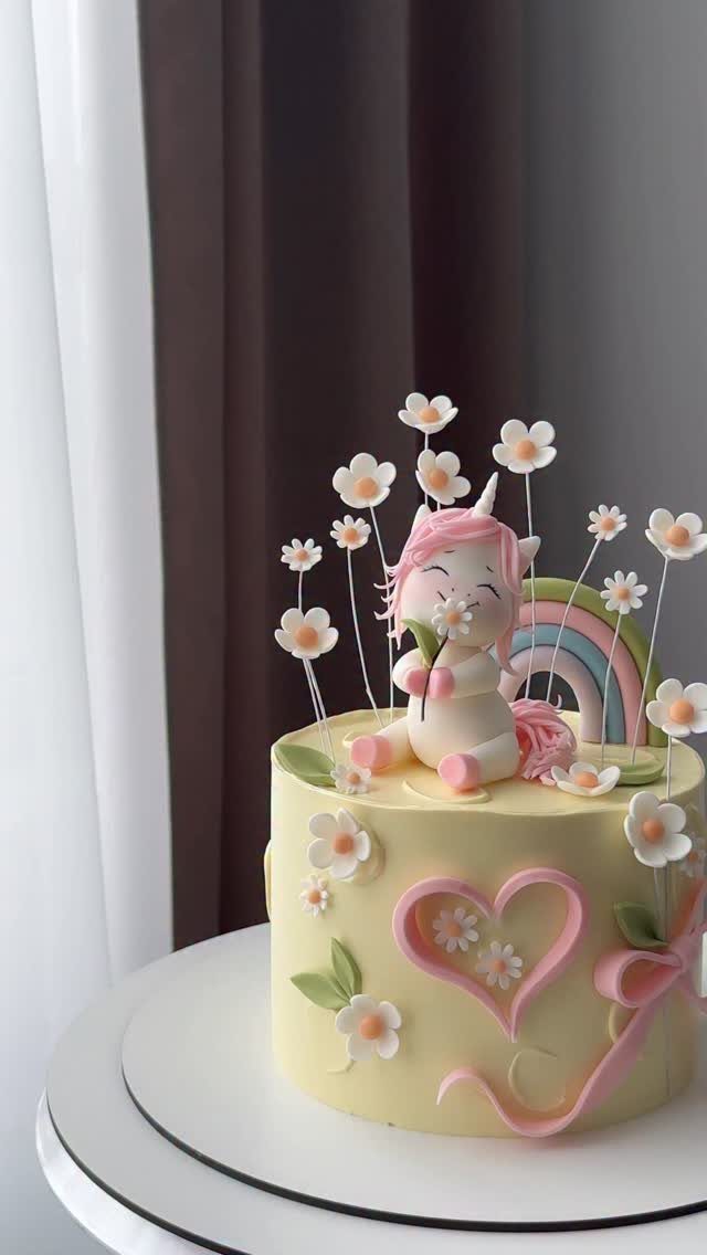 Yellow cake with a cute unicorn figurine, pink heart, and small rainbow decoration.